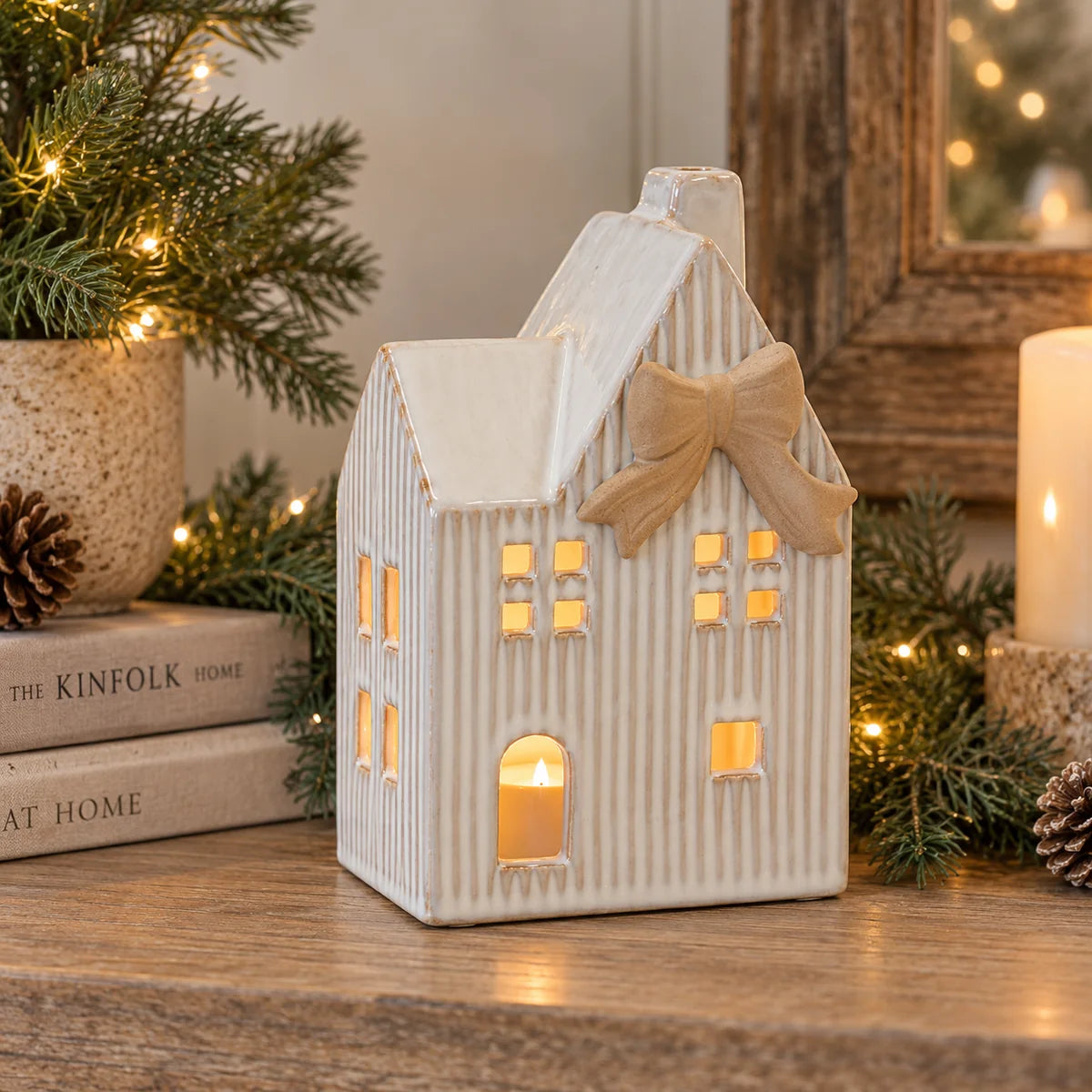 Large ceramic natural tealight Christmas house with cream bow glowing on rustic wooden festive console