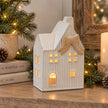 Large ceramic natural tealight Christmas house with cream bow glowing on rustic wooden festive console