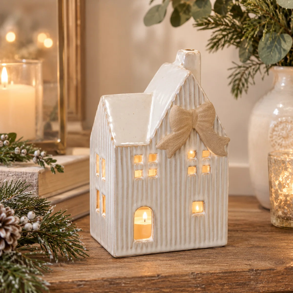 Ceramic Christmas cottage tealight holder with white ribbed walls and natural bow in warm country-home display