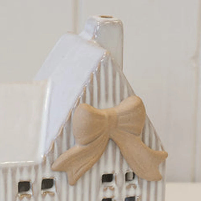 Close-up of ceramic natural bow and ribbed wall details on white Christmas tealight house