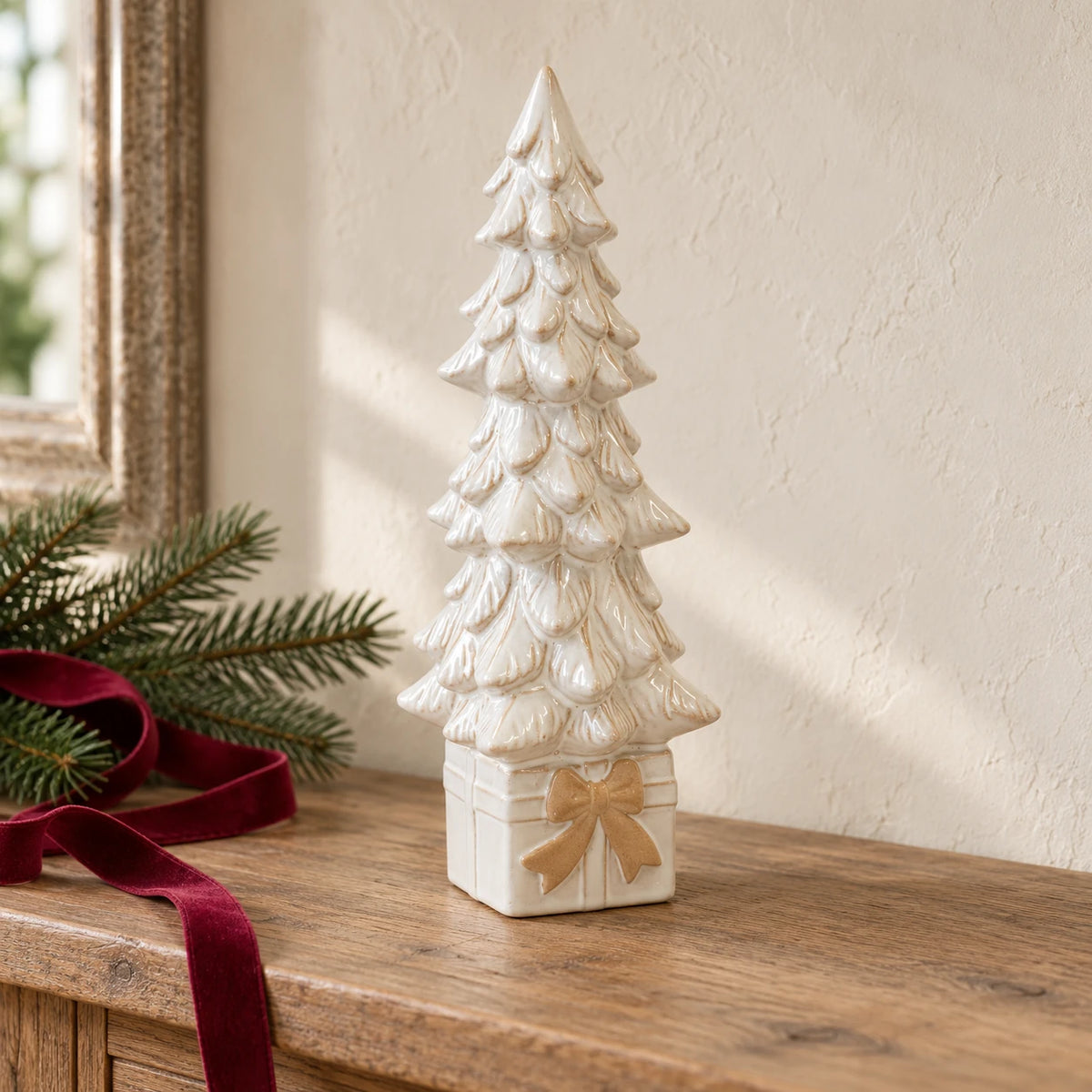 Large ivory ceramic Christmas tree on a gift-box base with beige bow, styled on an oak console.