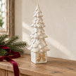 Large ivory ceramic Christmas tree on a gift-box base with beige bow, styled on an oak console.