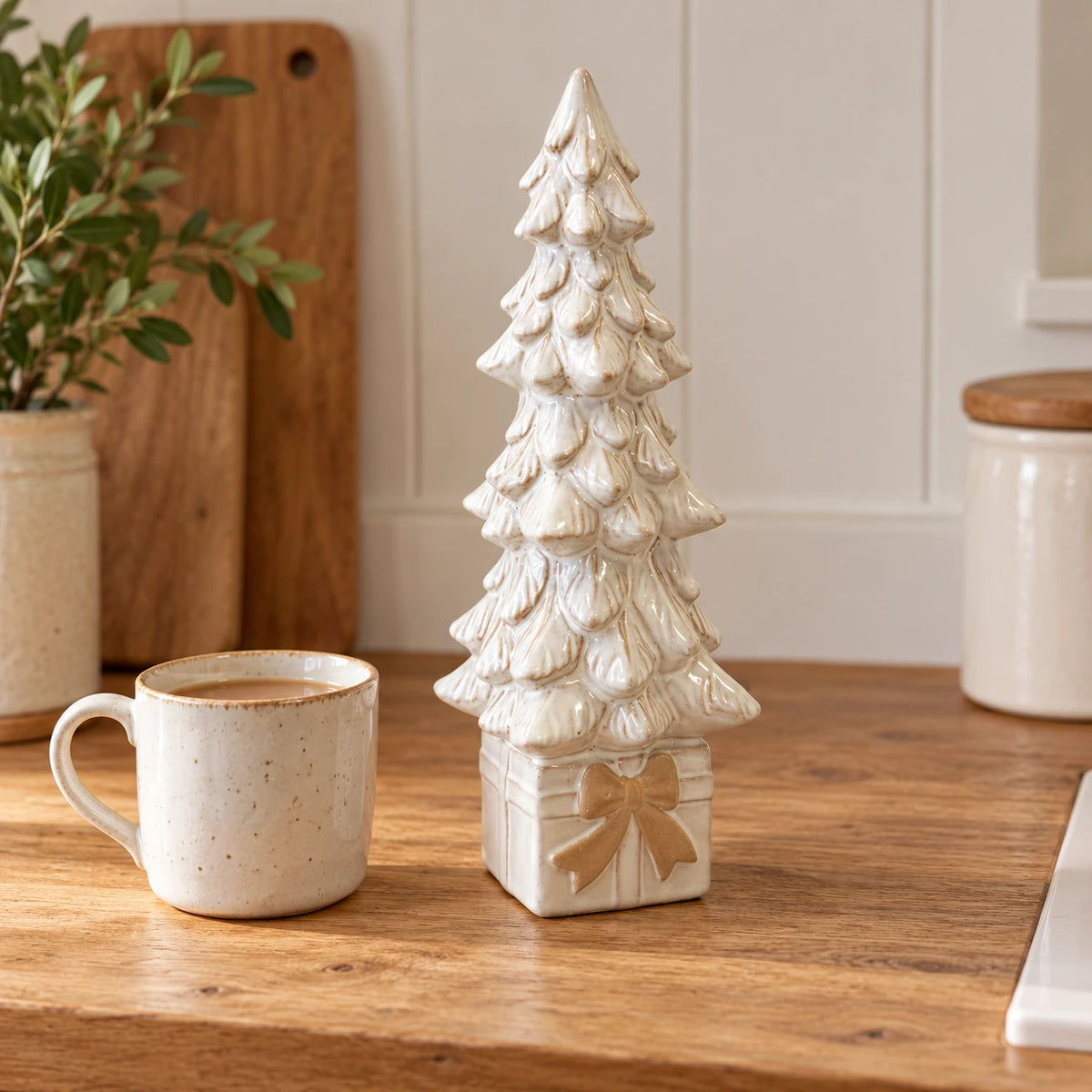 Thirty-centimetre ivory ceramic Christmas tree on a box beside a mug of tea.