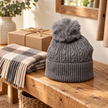 Charcoal cable knit bobble hat displayed on a rustic oak bench