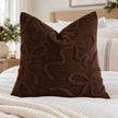 Chocolate brown bow bouclé cushion cover styled on white linen bedding