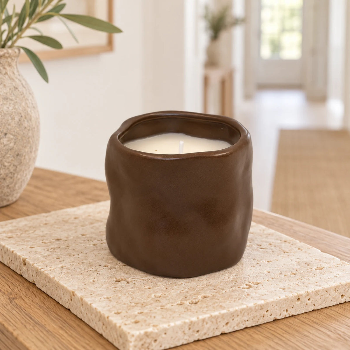 Chocolate brown sculpted ceramic candle, unlit on a pale stone tile on an oak console