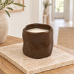 Chocolate brown sculpted ceramic candle, unlit on a pale stone tile on an oak console