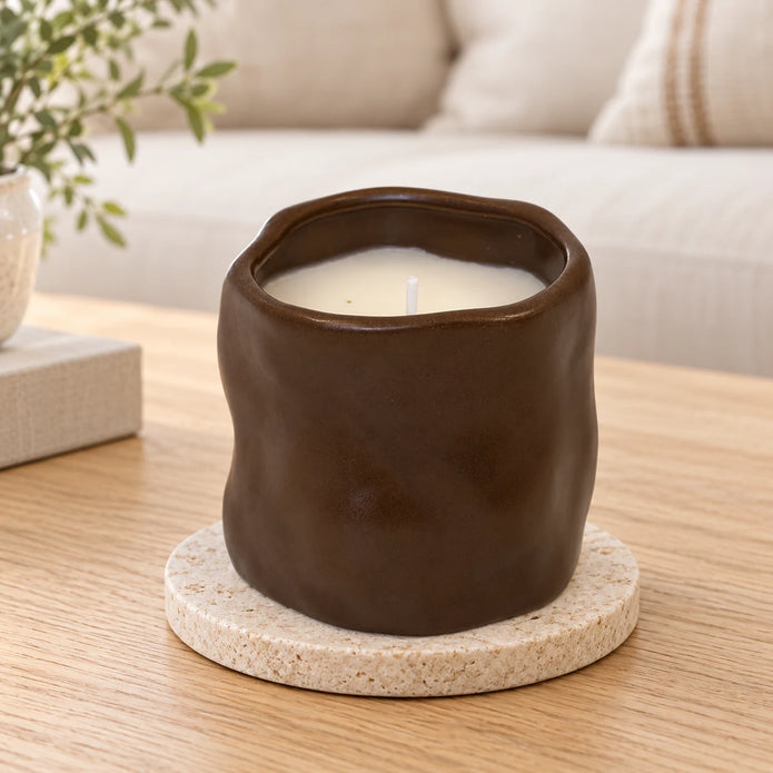 Unlit chocolate brown sculpted candle on a stone coaster in a bright neutral living room