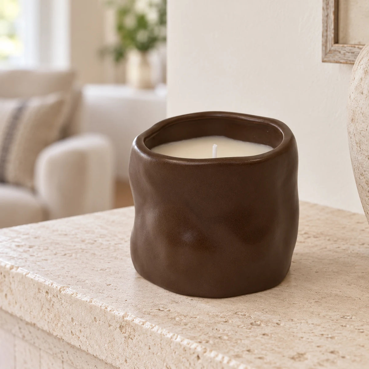 Unlit chocolate brown sculpted candle on a pale stone mantel