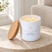 White Coconut and Sea Salt candle lit on a stone side table beside a linen armchair.
