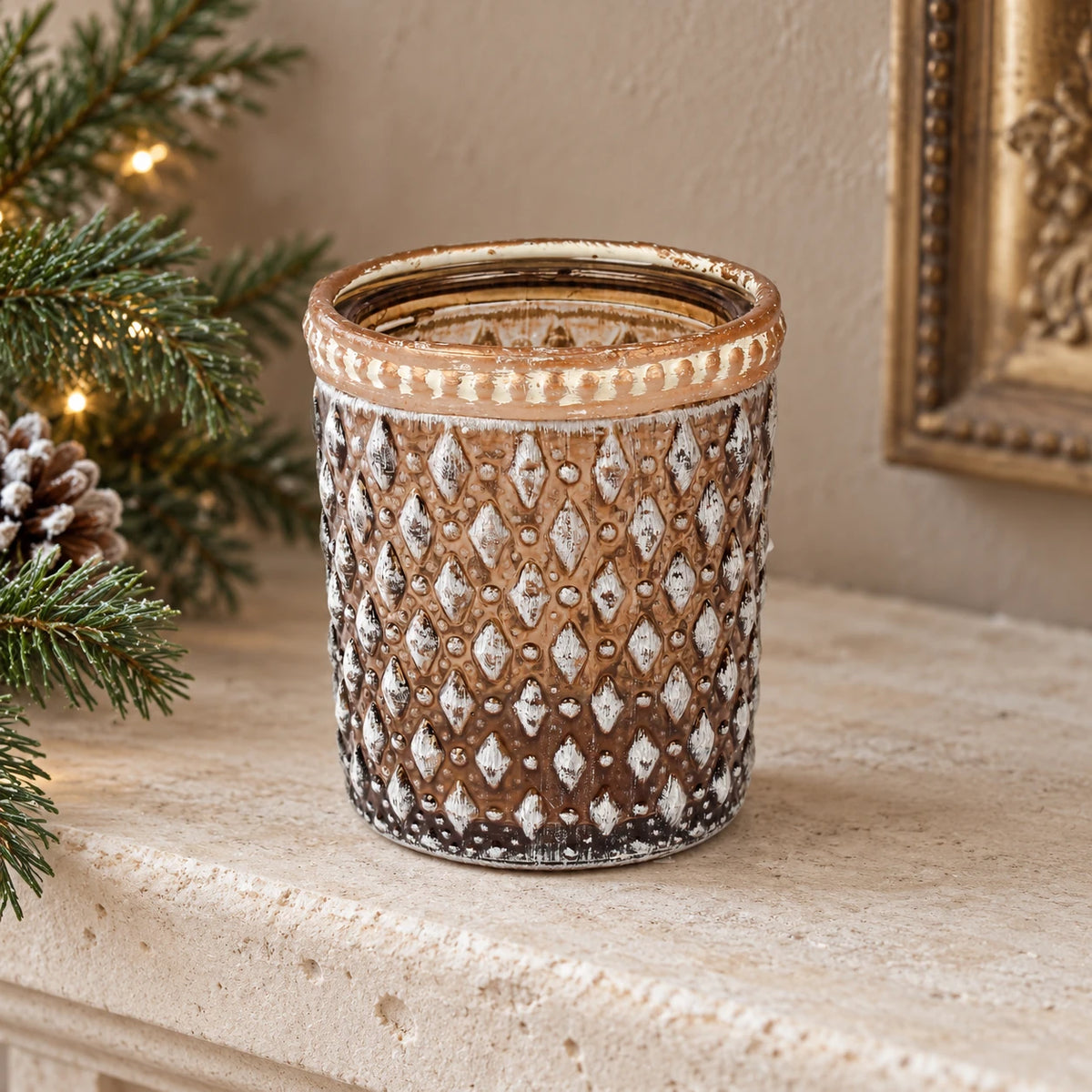Empty brown diamond glass tea light holder on a stone mantel beside Christmas greenery.