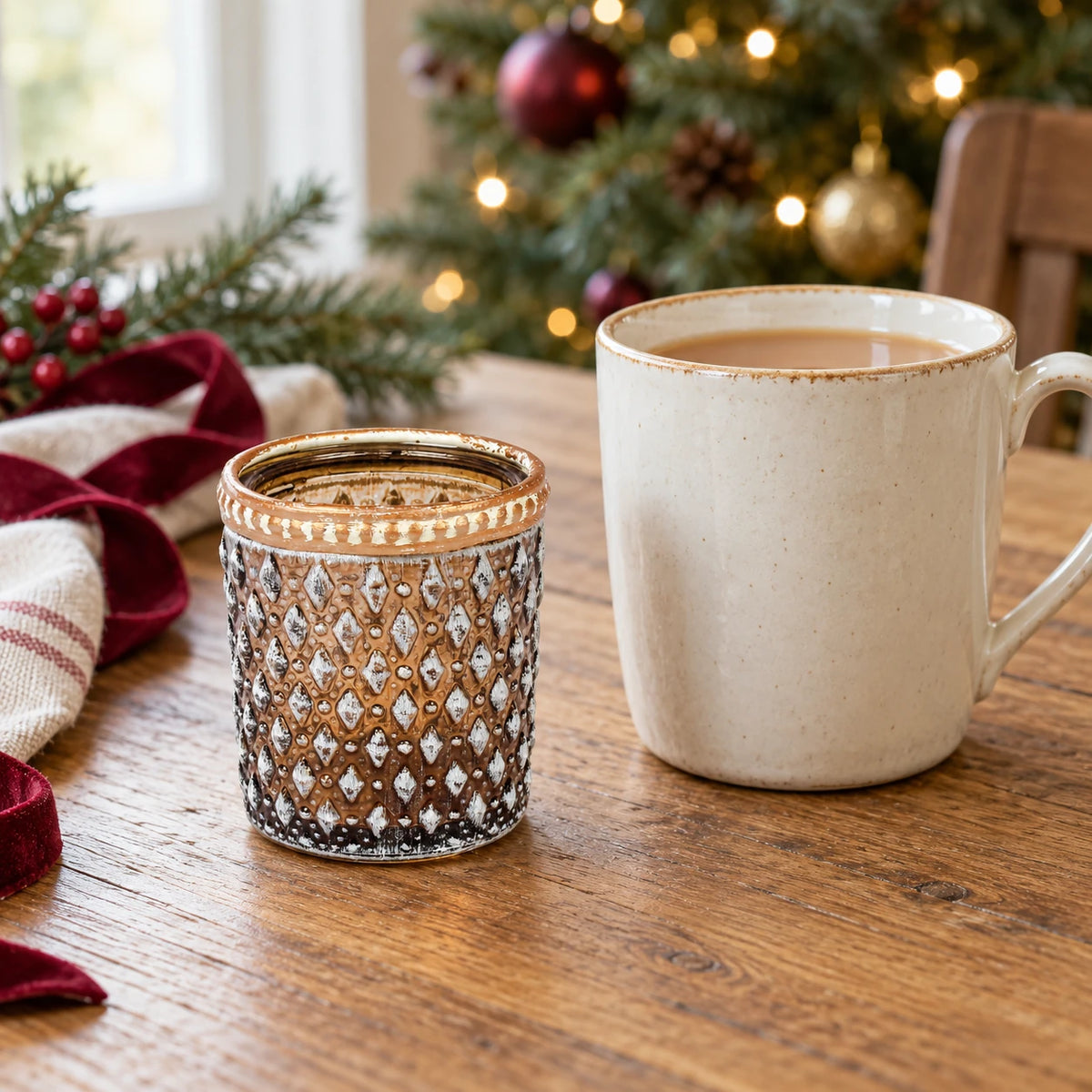 Small cognac glass tea light holder beside a mug of tea on a festive oak table.