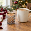 Small cognac glass tea light holder beside a mug of tea on a festive oak table.