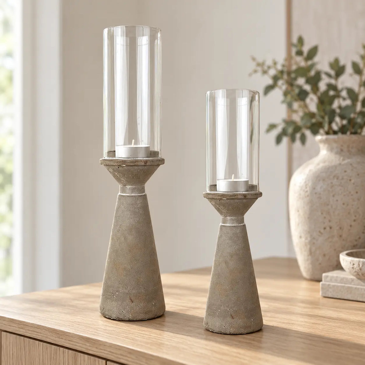 Two sizes of concrete hurricane holder with unlit white tealights on an oak sideboard