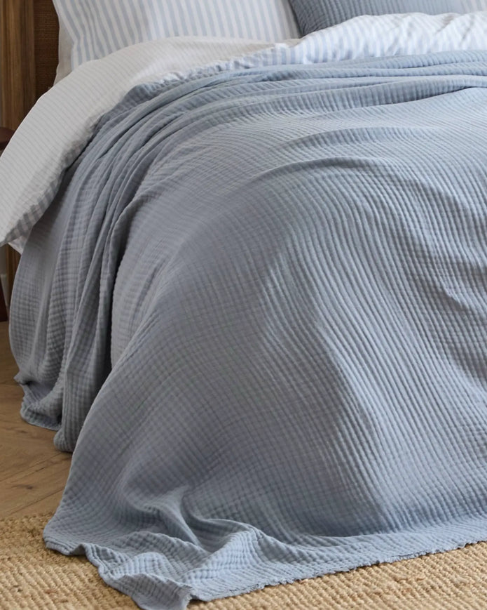 Ocean blue Riva Home muslin cotton throw bed cover, soft furnishings, showing folded lightweight fabric with textured weave.