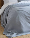 Ocean blue Riva Home muslin cotton throw bed cover, soft furnishings, showing folded lightweight fabric with textured weave.