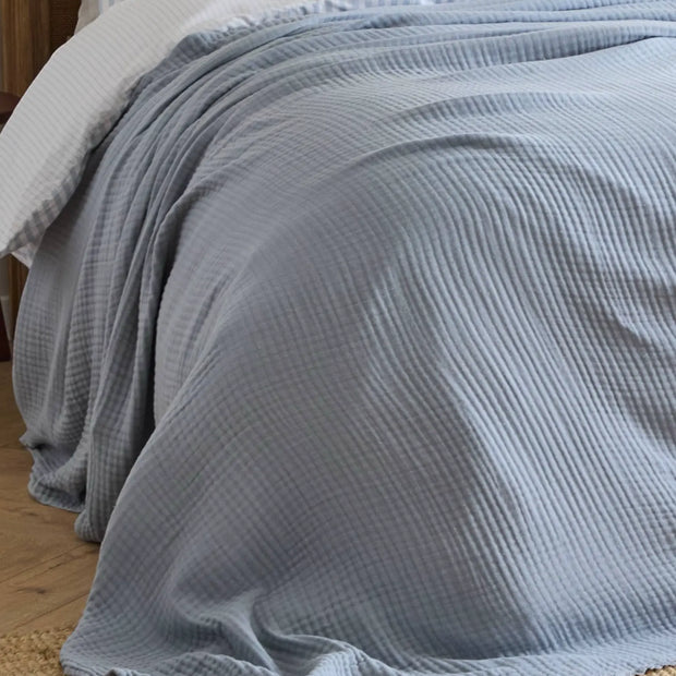Ocean blue Riva Home muslin cotton throw bed cover, soft furnishings, showing folded lightweight fabric with textured weave.