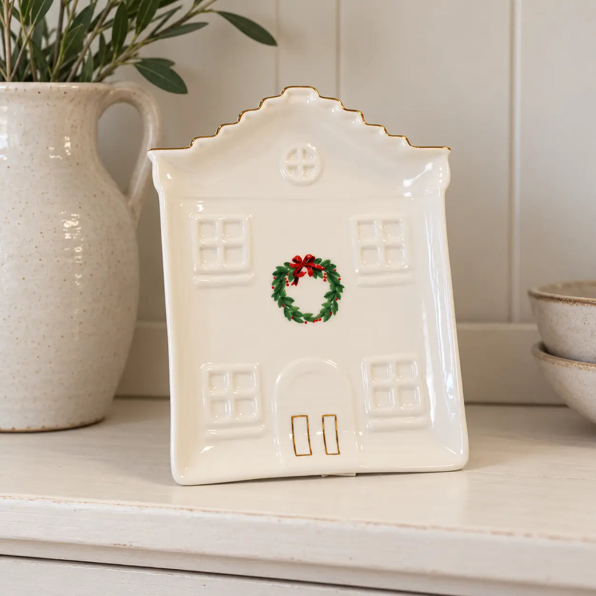 Cosy Christmas House Plate on a neutral dresser shelf beside a ceramic jug.