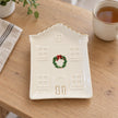 Empty house-shaped Christmas plate with gold edging on an oak table beside tea.