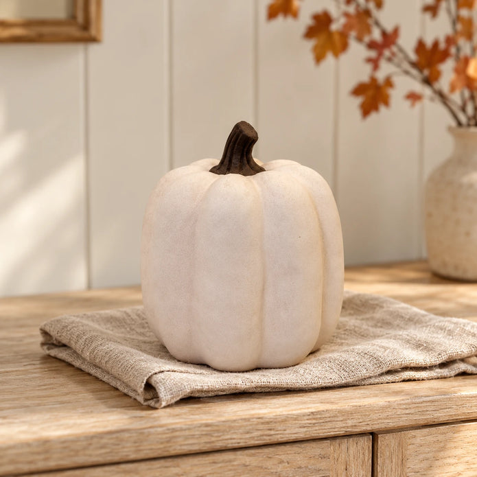 Cotton-white ceramic pumpkin with a dark stem on oatmeal linen and an oak sideboard