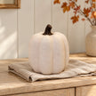 Cotton-white ceramic pumpkin with a dark stem on oatmeal linen and an oak sideboard