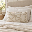 Cream and beige bow rectangle bouclé cushion cover styled upright against white sleeping pillows on a neutral bed.