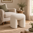 Cream boucle arched footstool beside a neutral armchair