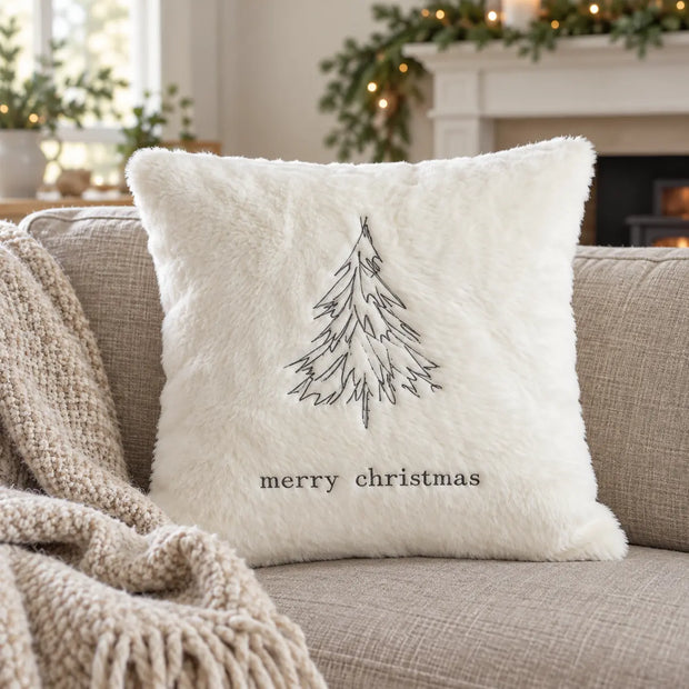 Cream embroidered fluffy Christmas tree cushion cover on a beige sofa beside a fireplace and lit tree