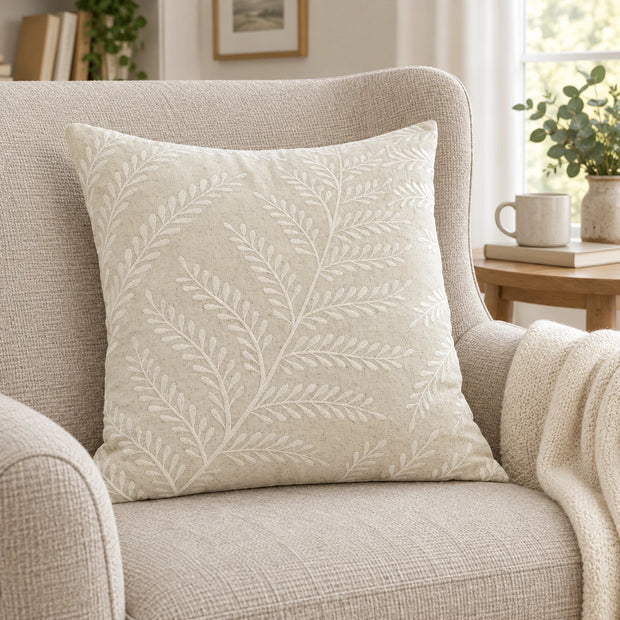 Cream Fern Embroidered Cushion Cover on an upholstered reading chair beside a cream throw.