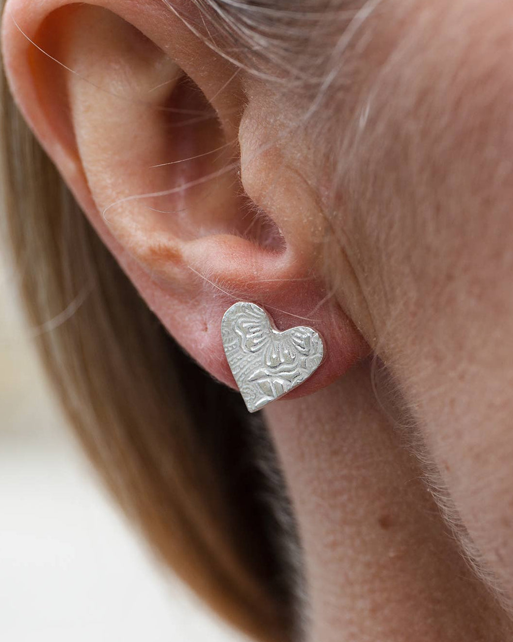 Silver heart-shaped earring worn by a person with a blurred background