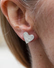 Silver heart-shaped earring worn by a person with a blurred background
