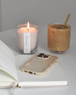 White scented candle in a clear sand jar with dark honey scent, part of The Candledust home fragrance collection.