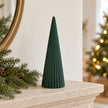 Dark green conical ceramic Christmas tree on a limestone mantel with seasonal greenery