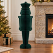 Deep green paper nutcracker beside a stone fireplace in a Christmas setting