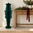 Deep green paper nutcracker standing beside an oak console with Christmas greenery