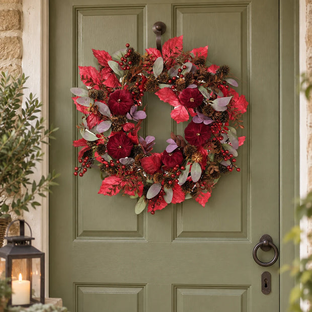 Deep red foliage and pumpkin wreath on an olive cottage door.