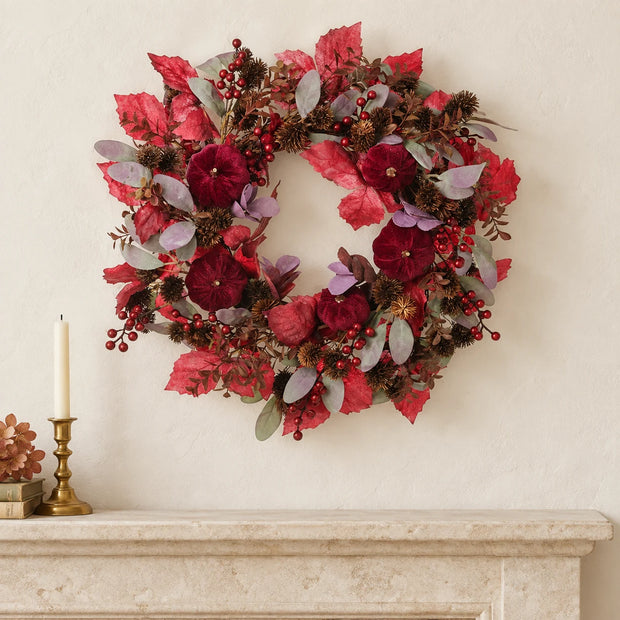 Deep red pumpkin wreath displayed above a cream stone mantel.