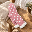 Pink spotted slipper socks with fluffy cuffs on a rustic oak bench