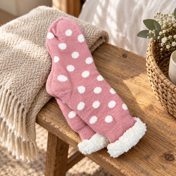 Pink spotted slipper socks with fluffy cuffs on a rustic oak bench