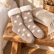 Taupe heart slipper socks with fluffy cuffs on a rustic oak bench