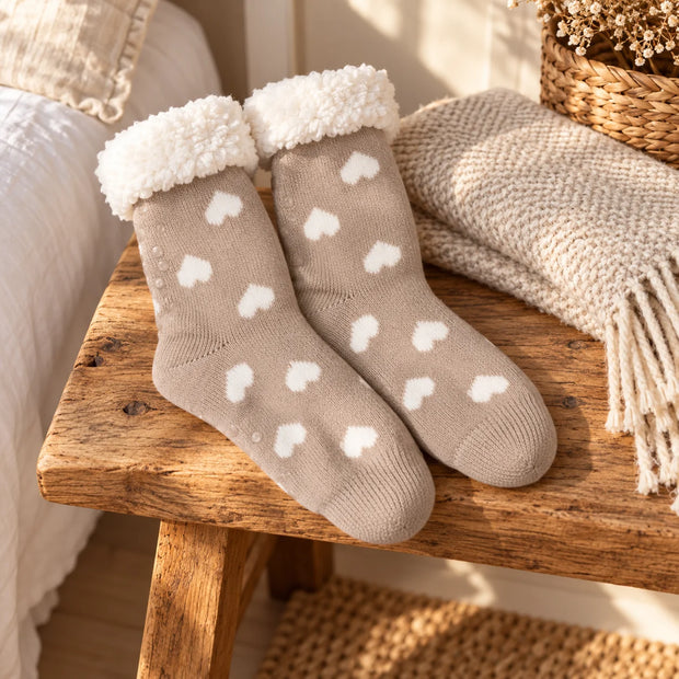 Taupe heart slipper socks with fluffy cuffs on a rustic oak bench