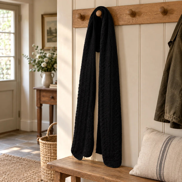 Black cable knit scarf hanging on an oak peg rail in a country hallway