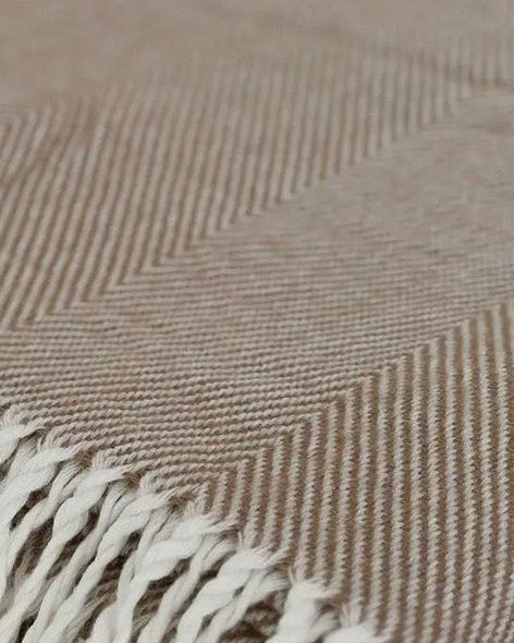Beige herringbone throw blanket with brown tassels, soft furnishings by Ellenvale Trade, draped over a surface showing texture and pattern.