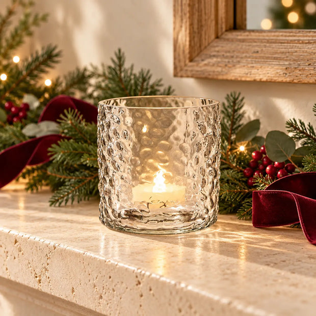 Esme clear dimpled glass lantern with glowing tealight on a Christmas mantel with greenery and burgundy ribbon.