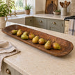 Extra-large rustic dough bowl holding green and russet pears on a cream kitchen island.