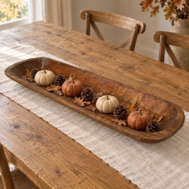 Extra-large wooden dough bowl styled with small pumpkins, pine cones and autumn leaves on a dining table.