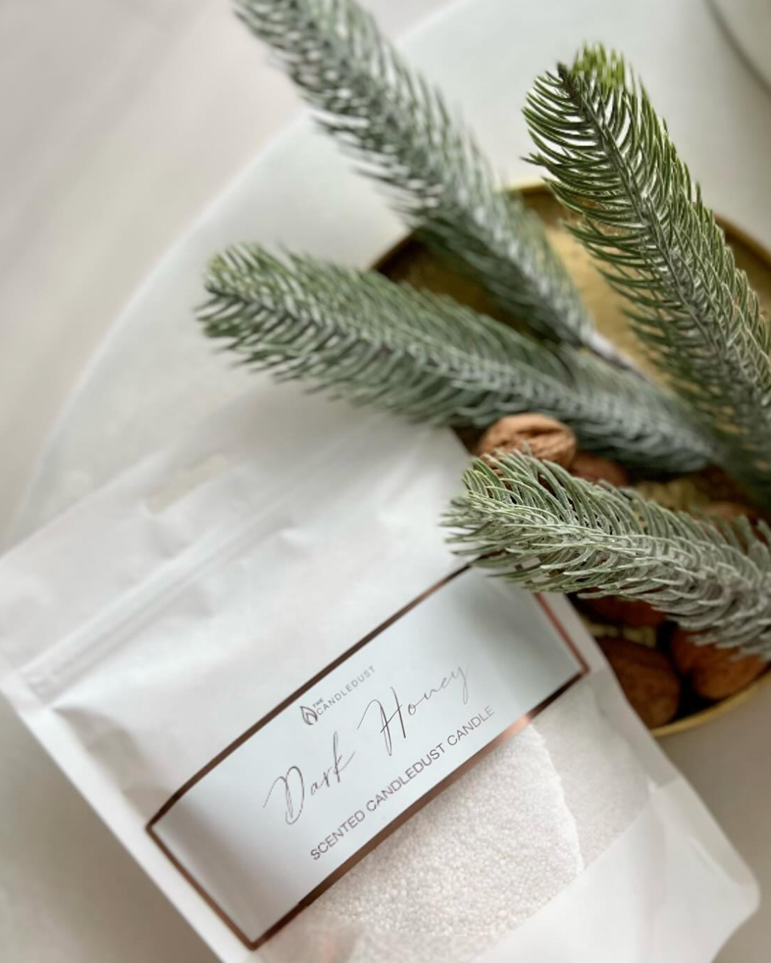 Scented candle packaging with a label and decorative greenery on a light surface