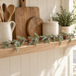 Delicate fir, berry and pinecone Christmas garland along an oak kitchen shelf