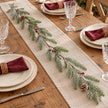 Faux green fir, red berry and pinecone garland on a Christmas dining table with burgundy napkins