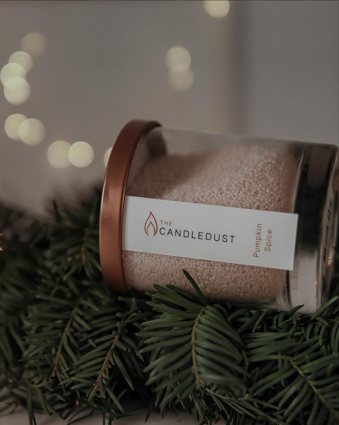 Candle in a decorative container with a label on a branch with blurred lights in the background